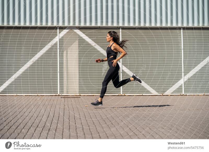 Junge Joggerin rennt vor einer Mauer rennen Muße fit gesund Gesundheit Jogging Dynamik dynamisch Power Anreiz Ansporn Antrieb motivieren motiviert außen draußen