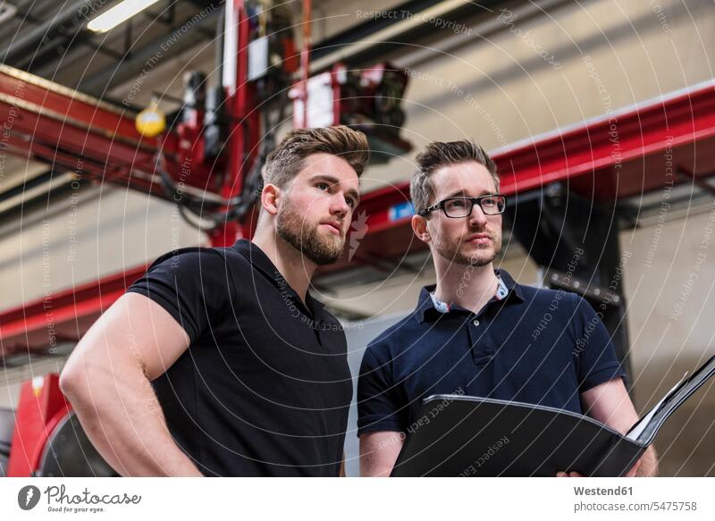 Zwei Männer mit Ordner in der Fabrikhalle, die sich umsehen Produktionshalle Montagehalle Kollegen Arbeitskollegen Fabriken umherblicken umschauen Mappe Mappen