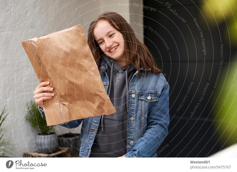 Mädchen steht vor dem Haus und freut sich über ein Paket Pakete Päckchen Nachricht Nachrichten freuen außen draußen im Freien am Tag Tagesaufnahme