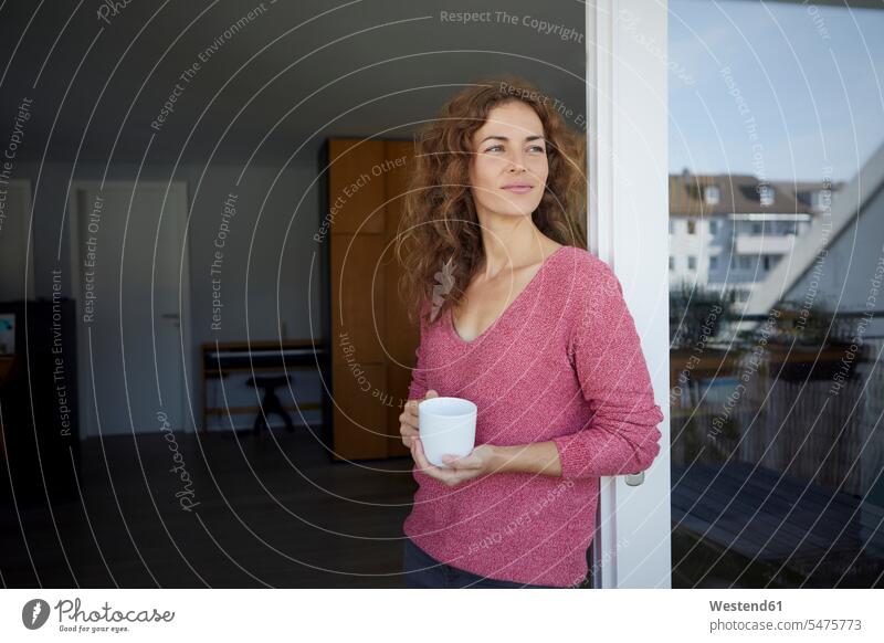 Schöne Frau hält Kaffeetasse in der Hand, während sie sich zu Hause an die Tür lehnt Farbaufnahme Farbe Farbfoto Farbphoto Tag Tageslichtaufnahme