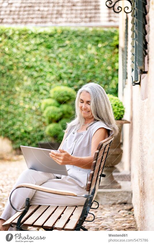 Frau mit langen grauen Haaren sitzt auf einer Bank im Landhaus und benutzt ein Tablet Tablet Computer Tablet-PC Tablet PC iPad Tablet-Computer Sitzbänke Bänke