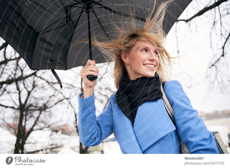 Lächelnde blonde Frau hält Regenschirm im Sturm Schals Schirme Regenschirme freuen Frohsinn Fröhlichkeit Heiterkeit geniessen Genuss Glück glücklich sein