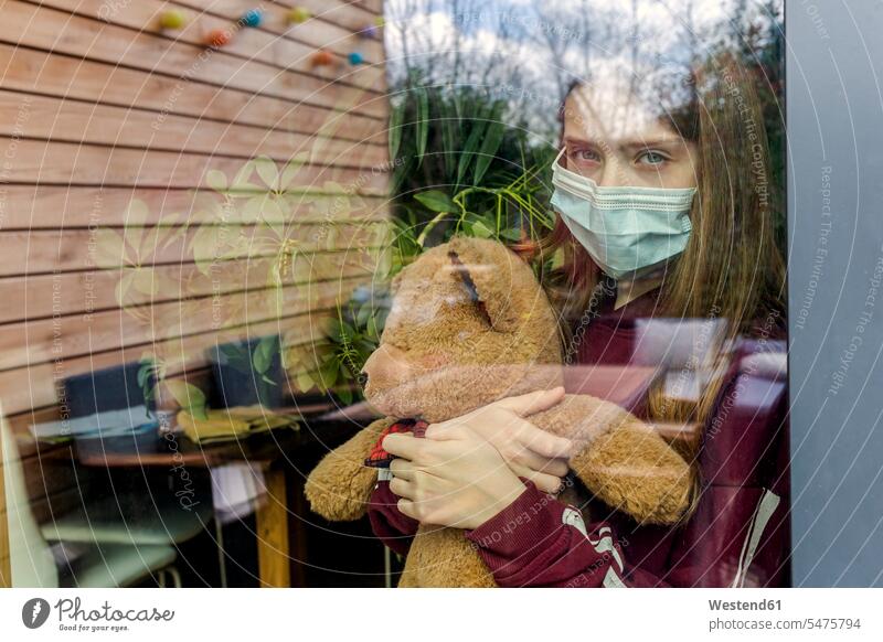 Bildnis eines Mädchens mit chirurgischer Maske und Teddybär hinter Fensterscheibe Fensterscheiben Teddies Teddybaer Teddybaeren Teddybären pessimistisch