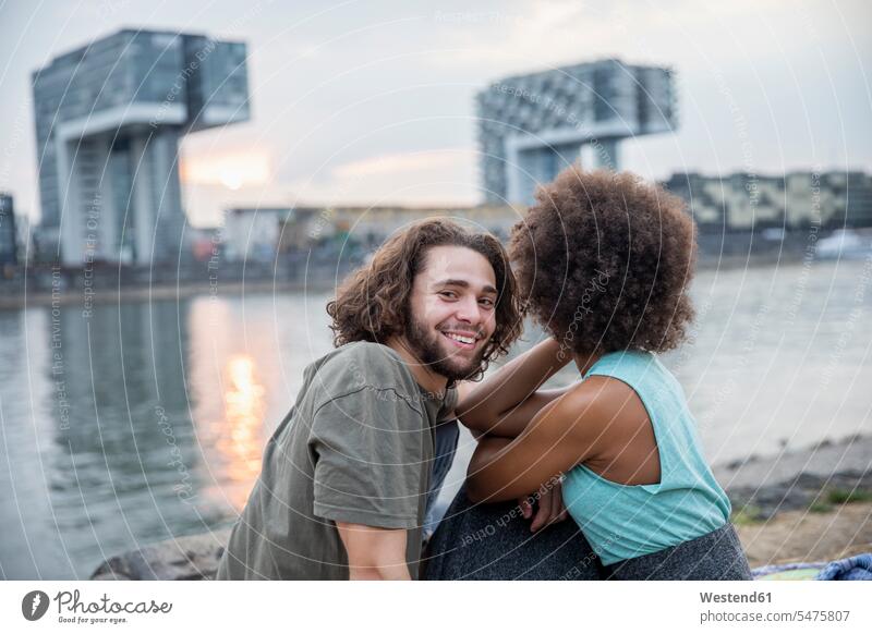 Deutschland, Köln, glückliches Paar entspannt am Flussufer bei Sonnenuntergang entspanntheit relaxt Pärchen Paare Partnerschaft Sonnenuntergänge Ufer