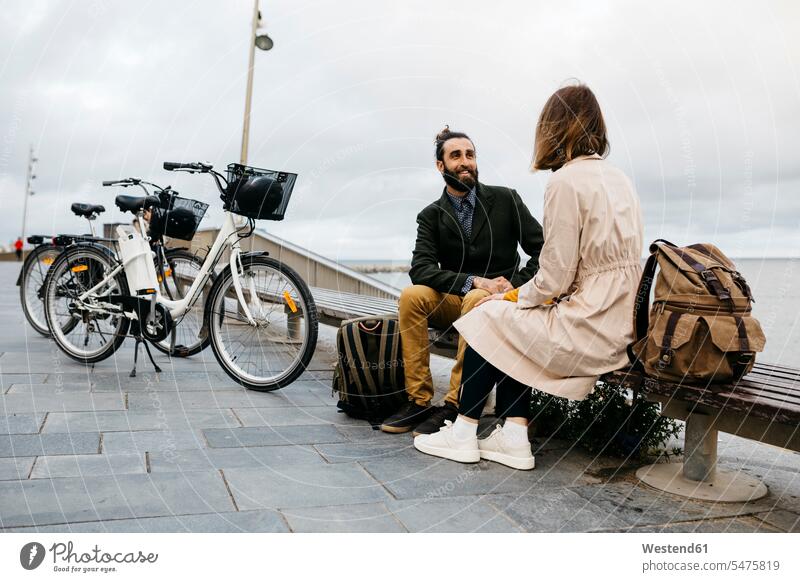 Paar sitzt auf einer Bank an der Strandpromenade neben E-Bikes im Gespräch Strandpromenaden eBikes Elektrofahrrad Elektrorad sprechen reden sitzen sitzend