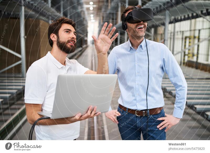 Mann mit Laptop und Geschäftsmann mit VR-Brille in Fabrik Arbeitskollege Arbeitskollegen Kollege Job Berufe Berufstätigkeit Beschäftigung Jobs geschäftlich