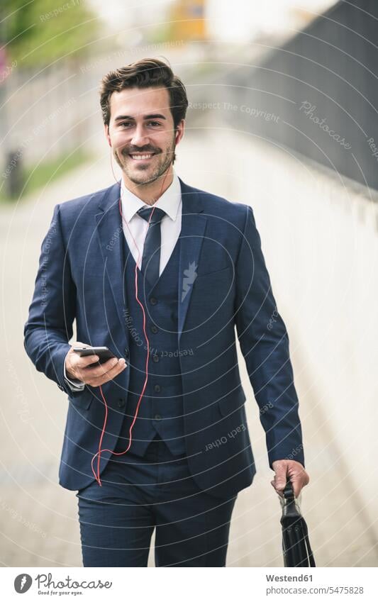 Geschäftsmann zu Fuß in der Stadt mit Handy und Kopfhörer Freiberufler freiberuflich freie Berufe Business Geschäftsleben Geschäftswelt geschäftlich Urban