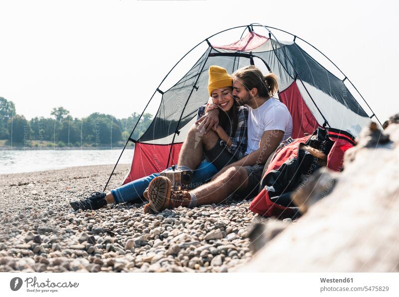 Glückliches junges Paar sitzt in einem Zelt am Flussufer Pärchen Paare Partnerschaft Zelte glücklich glücklich sein glücklichsein sitzen sitzend lächeln Mensch