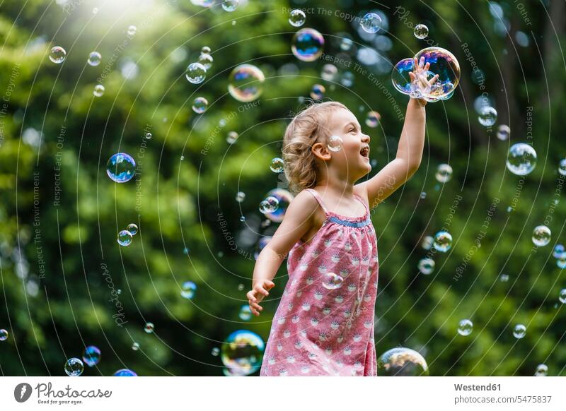 Fröhliches Mädchen inmitten von Blasen im Park Farbaufnahme Farbe Farbfoto Farbphoto Außenaufnahme außen draußen im Freien Tag Tageslichtaufnahme