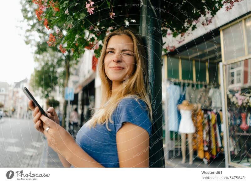 Niederlande, Maastricht, lächelnde junge Frau mit Handy in der Stadt blinkt blinzeln Mobiltelefon Handies Handys Mobiltelefone staedtisch städtisch weiblich