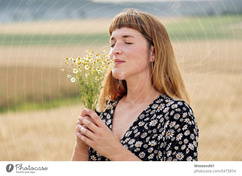 Lächelnde junge Frau mit geschlossenen Augen riechen Strauß Kamille Blume in der Natur Leute Menschen People Person Personen erwachsen Erwachsene Frauen