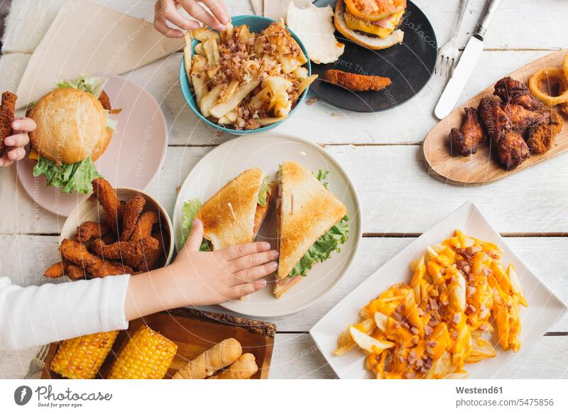 Kinderhände auf einem Tisch voller amerikanischer Lebensmittel Kids Tische Hand Hände Mensch Menschen Leute People Personen Burger Hunger hungrig Pommes Frites