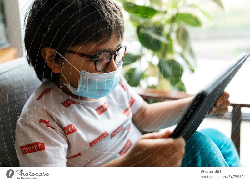 Junge mit chirurgischer Maske auf Sessel sitzend mit digitalem Tablett Leute Menschen People Person Personen Europäisch Kaukasier kaukasisch 1 Ein ein Mensch