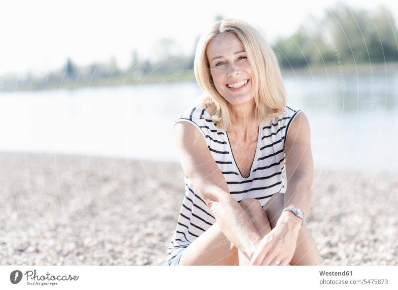 Porträt einer glücklichen reifen Frau, die am Flussufer sitzt Deutschland ausruhen Rast Erholung erholen Top Tops offenes Lächeln lachen offenes Laecheln
