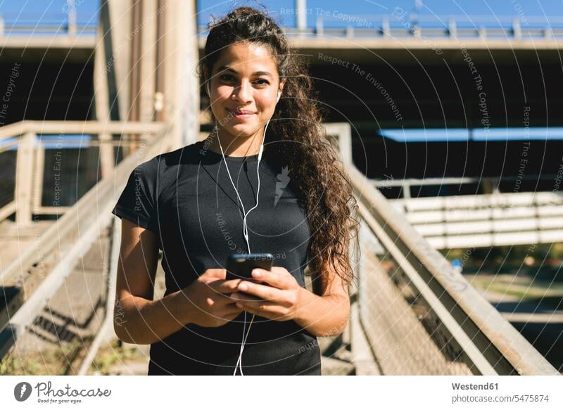 Porträt einer sportlichen jungen Frau, die eine Pause macht und Musik hört weiblich Frauen Portrait Porträts Portraits hören hoeren Sport Erwachsener erwachsen