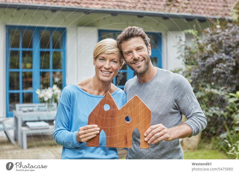 Porträt eines lächelnden Paares, das vor dem Modell seines Wohnhauses steht Modelle Portrait Porträts Portraits stehen stehend Haus Häuser Haeuser Pärchen