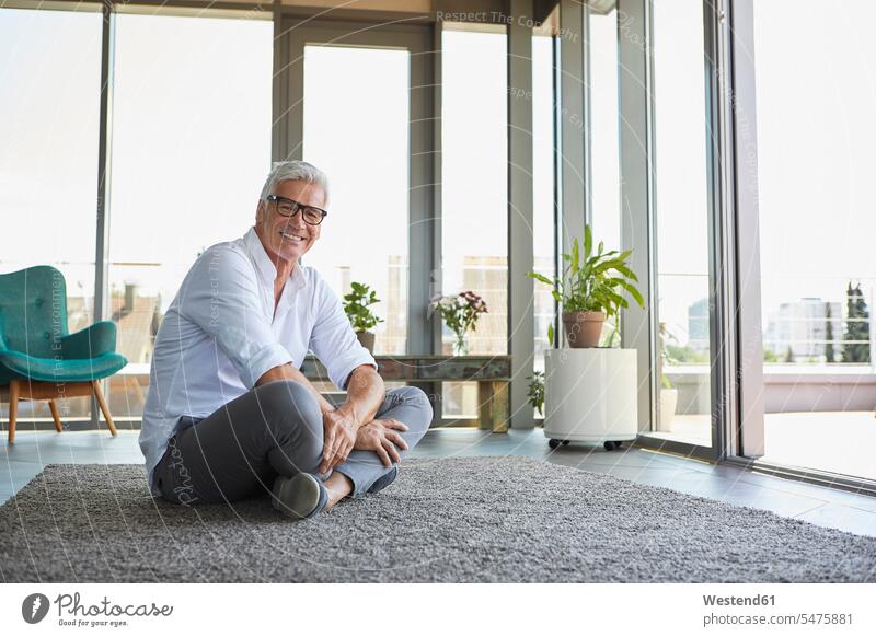 Lächelnd reifen Mann entspannt sitzen auf Teppich zu Hause Männer männlich entspanntheit relaxt sitzend sitzt lächeln Teppiche Zuhause daheim Erwachsener