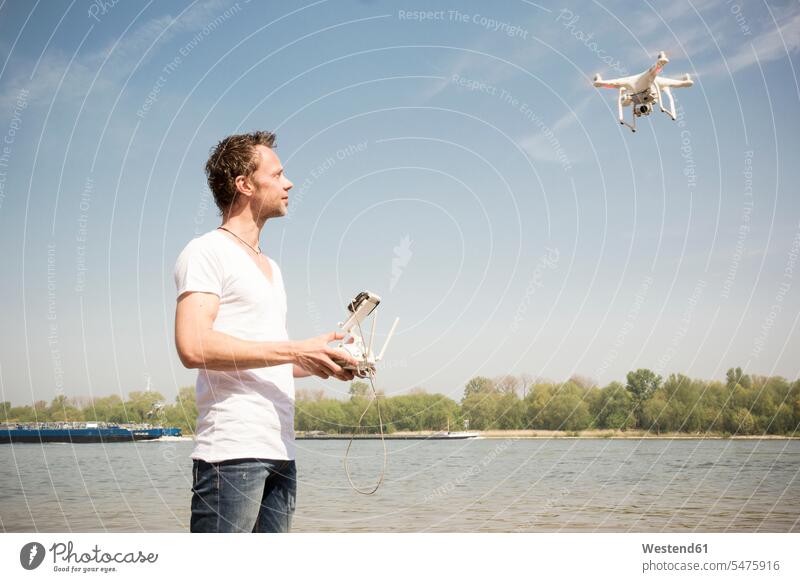 Mann fliegt Drohne an einem Fluss Drohnen fliegen fliegend Fluesse Fluß Flüsse Männer männlich Gewässer Wasser Erwachsener erwachsen Mensch Menschen Leute