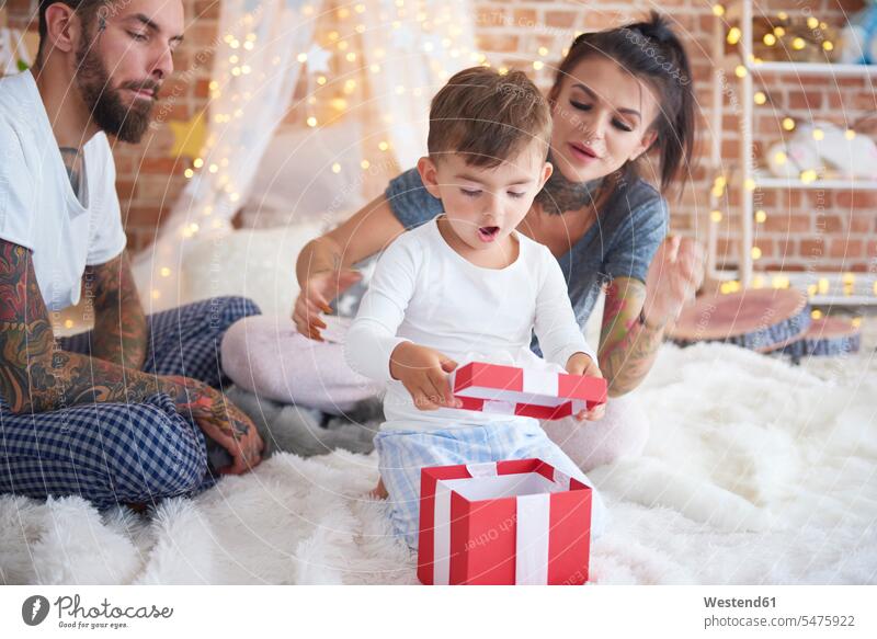Überrascht Junge öffnen Weihnachtsgeschenk mit seinen Eltern im Bett Weihnachtsgeschenke Familie Familien oeffnen überrascht erstaunt verwundert verblüfft