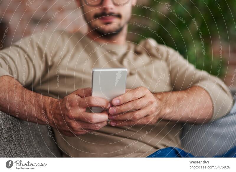 Mann sitzt auf Couch Textnachrichten, Teilansicht Männer männlich Zuhause zu Hause daheim SMS sitzen sitzend Sofa Couches Liege Sofas Erwachsener erwachsen