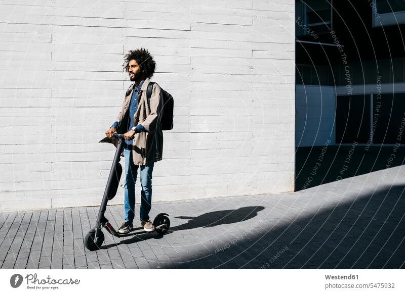Mann mit Rucksack auf E-Scooter stehend Rucksäcke steht Muße mobil außen draußen im Freien staedtisch städtisch Urbanitaet Urbanität Trends auf Achse