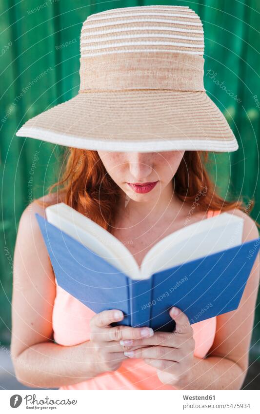 Rothaarige junge Frau vor grüner Holztür liest ein Buch im Sommer Bücher Lektüre sommerlich Sommerzeit Muße Fashion modisch Attraktivität gut aussehend