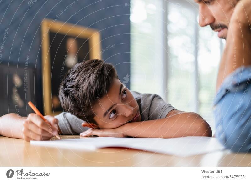 Vater hilft Sohn bei den Hausaufgaben Schüler Tisch Stift lernen schreiben sitzen Zuhause Gemeinsam Kontrolle Lifestyle Unterstützung Verantwortung