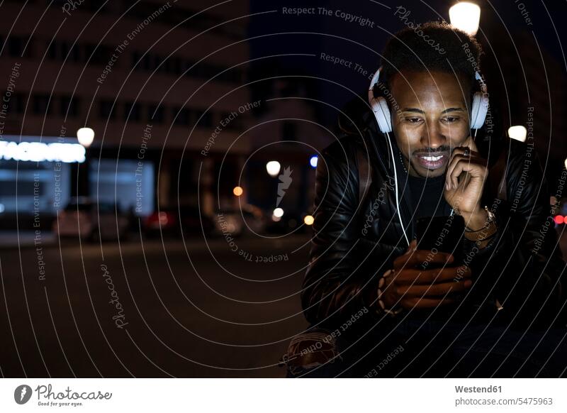 Mann in der Stadt in der Nacht mit Smartphone und Kopfhörern Informationen Jacken Kopfhoerer Telekommunikation telefonieren Handies Handys Mobiltelefon