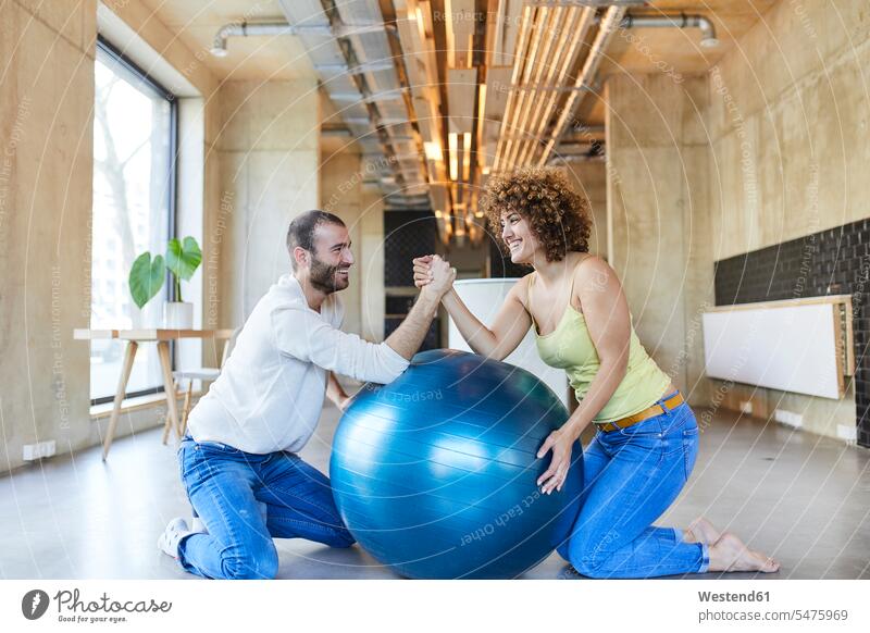 Glücklicher Mann und Frau Armdrücken auf Fitness-Ball in modernen Büro knien armdrücken armdruecken Arm drücken Spaß Spass Späße spassig Spässe spaßig