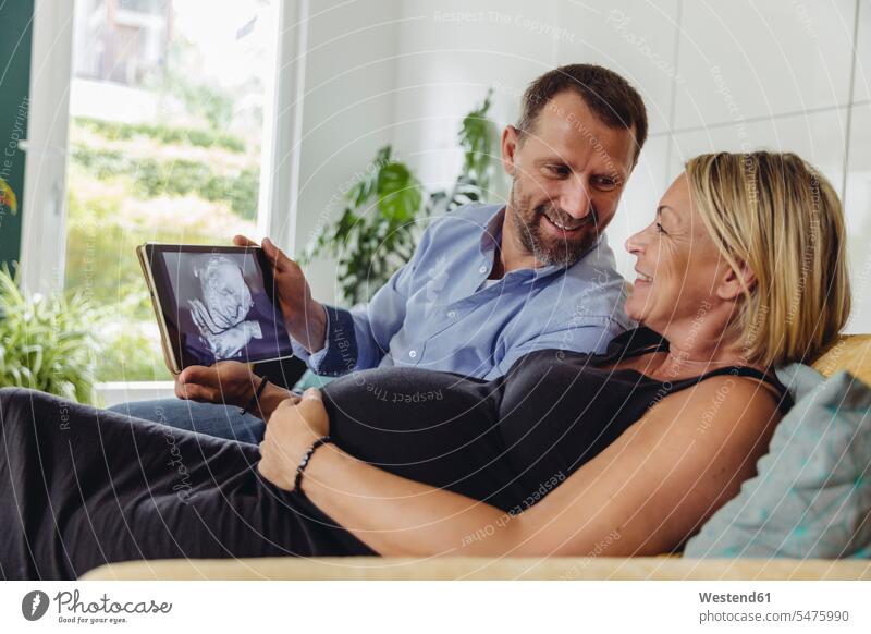 Älteres schwangeres Paar betrachtet ein 3D-Bild ihres ungeborenen Kindes auf einem Tablet-Computer Schwangere schwangere Frau ansehen Bildnis Bilder schauen