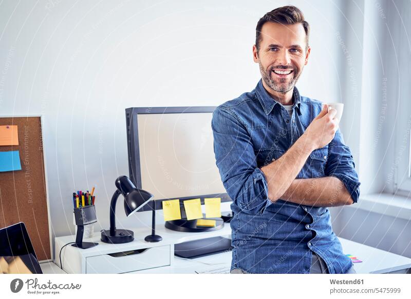 Porträt eines lächelnden Mannes mit Tasse Kaffee am Schreibtisch im Büro Portrait Porträts Portraits Männer männlich Arbeitstisch Schreibtische Office Büros
