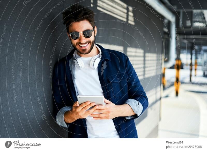 Porträt eines lächelnden jungen Mannes, der an der Wand lehnt und auf ein digitales Tablet schaut anlehnen angelehnt lehnend Tablet Computer Tablet-PC Tablet PC