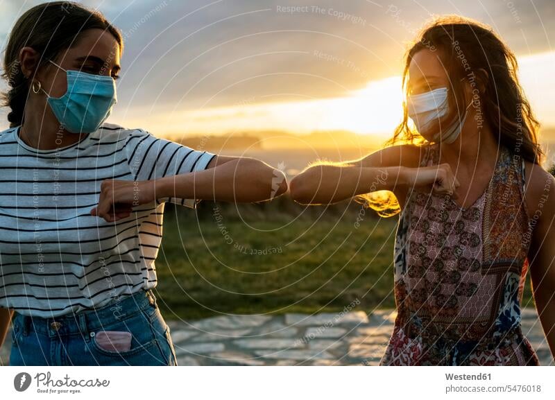 Junge Frauen mit schützenden Gesichtsmasken, die während COVID-19 mit dem Ellbogen gegen den Himmel stoßen Farbaufnahme Farbe Farbfoto Farbphoto Außenaufnahme