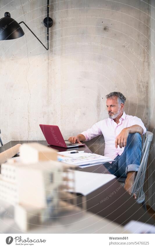 Geschäftsmann in einem Loft mit Laptop mit Dokumenten und Architekturmodell auf dem Tisch Notebook Laptops Notebooks Tische Businessmann Businessmänner