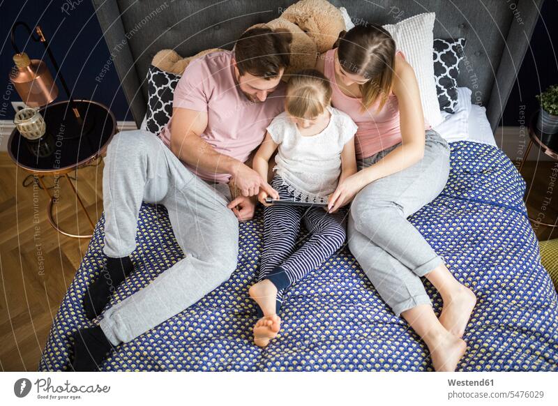 glückliche Familie sitzt auf dem Bett und schaut etwas auf dem digitalen Tablet mit der kleinen Tochter Töchter Familien ansehen zuschauen Tablet Computer