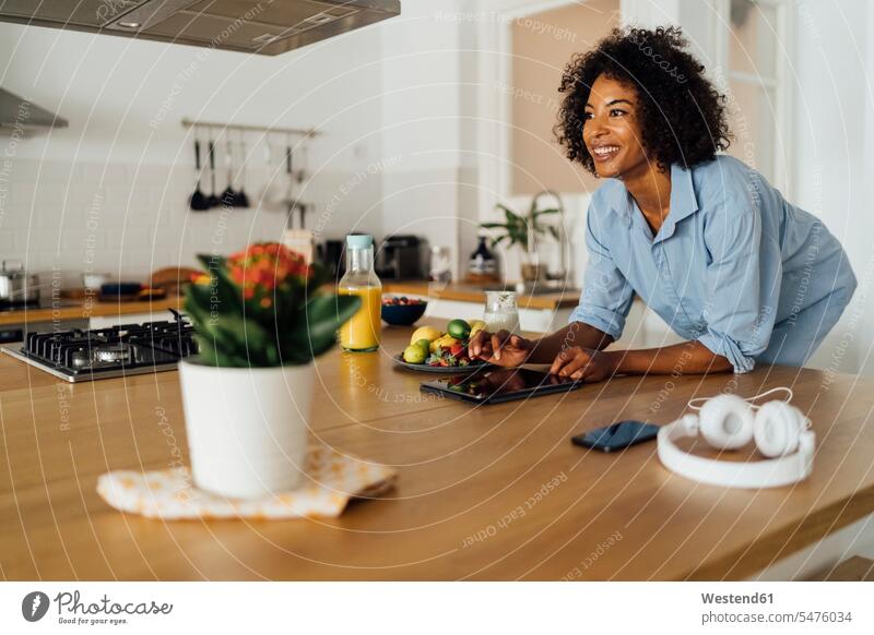 Frau mit digitalem Tablet und mit einem gesunden Frühstück in ihrer Küche frühstücken lächeln Obst Früchte stehen stehend steht benutzen benützen morgens Morgen