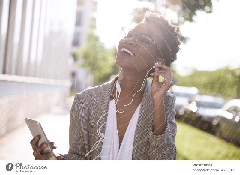 Porträt einer glücklichen Geschäftsfrau mit Smartphone und Kopfhörern Ohrhörer lachen Portrait Porträts Portraits Geschäftsfrauen Businesswomen Businessfrauen