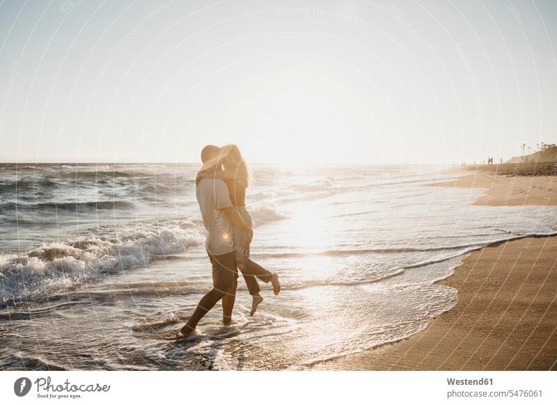 Liebenswertes junges Paar umarmt sich bei Sonnenuntergang am Meeresufer Leute Menschen People Person Personen Europäisch Kaukasier kaukasisch 2 2 Menschen