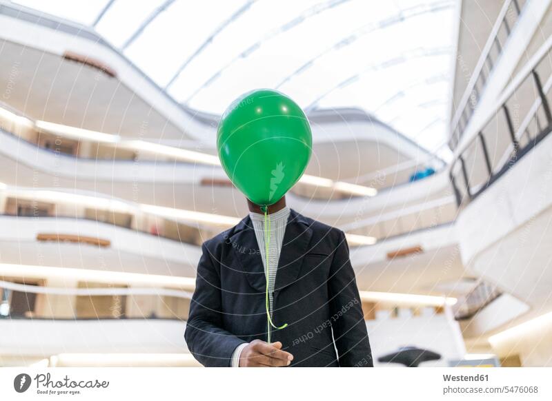 Älterer Geschäftsmann versteckt Gesicht hinter grünem Ballon Businessmann Businessmänner Geschäftsmänner Mann Männer männlich verstecken Luftballons Ballons