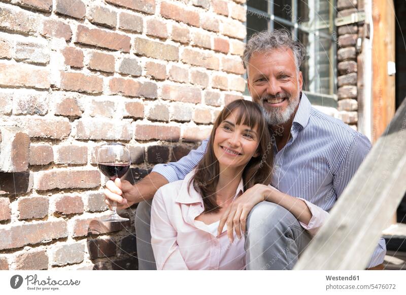 Reifes Paar, das auf einer Treppe sitzt und Wein trinkt Ziegelmauer Ziegelwand Backsteinmauer Treppenaufgang sitzen sitzend Pärchen Paare Partnerschaft lachen