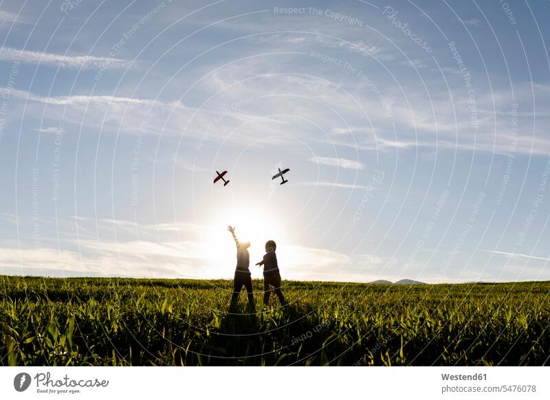 Verspielte Brüder fliegen Flugzeugspielzeug, während sie auf Gras in der Wiese stehen Farbaufnahme Farbe Farbfoto Farbphoto Außenaufnahme außen draußen