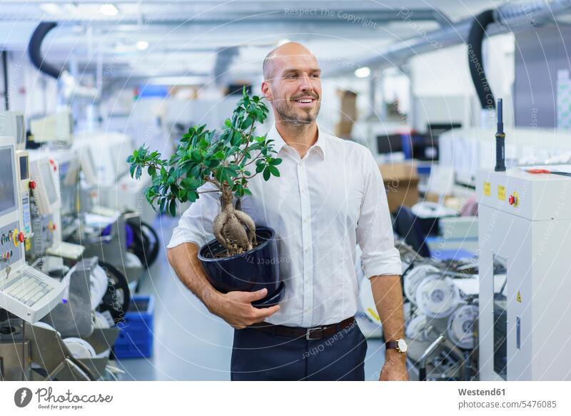 Lächelnder Geschäftsmann hält Topfpflanze, während er auf die Fabrik schaut Farbaufnahme Farbe Farbfoto Farbphoto Innenaufnahme Innenaufnahmen innen drinnen