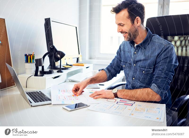 Lächelnder Webdesigner arbeitet am Schreibtisch im Büro an einem Entwurf Arbeitstisch Schreibtische Office Büros Mann Männer männlich arbeiten lächeln Skizze
