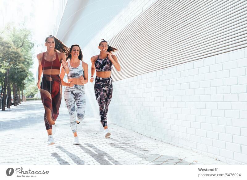 Rückansicht von drei sportlichen jungen Frauen, die in der Stadt laufen Freunde Kameradschaft Freundin rennen sommerlich Sommerzeit freuen Frohsinn Fröhlichkeit