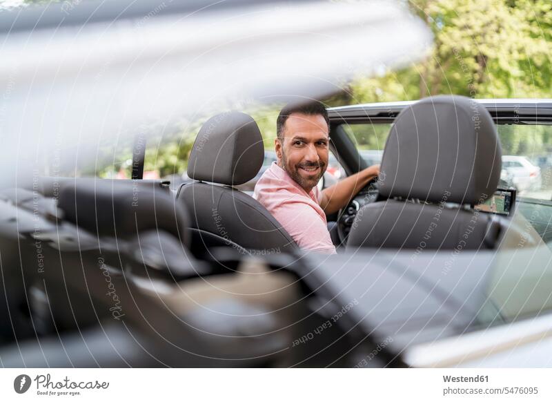 Mann sitzend im Auto mit schließendem Cabrioverdeck Autofahrer Kraftfahrer Freizeitkleidung casual Freizeitbekleidung Wohlstand Vermögen Reichtum reich