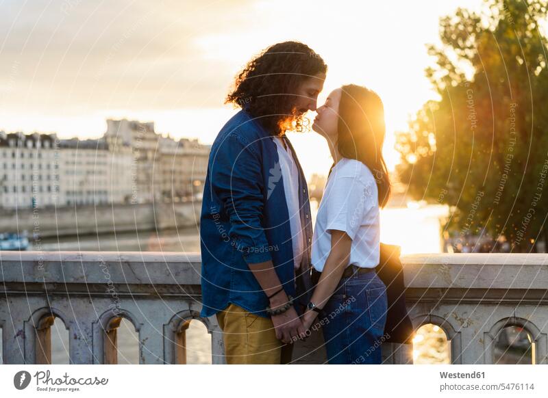 Frankreich, Paris, liebevolles junges Paar am Fluss Seine bei Sonnenuntergang Zuneigung Sonnenuntergänge Pärchen Paare Partnerschaft Fluesse Fluß Flüsse