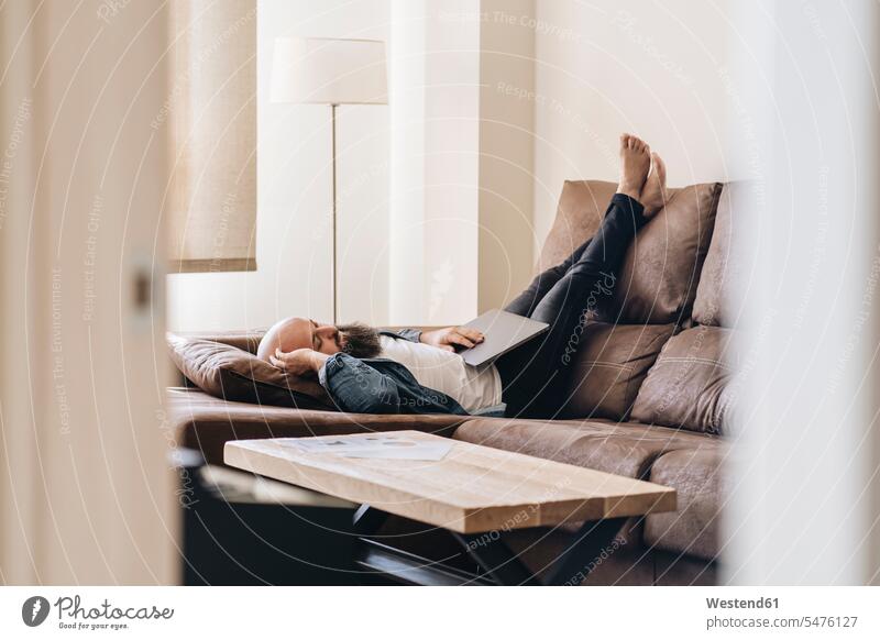 Mann macht ein Nickerchen, während er mit Laptop auf dem Sofa zu Hause liegt Farbaufnahme Farbe Farbfoto Farbphoto Freizeitkleidung Freizeitbekleidung casual