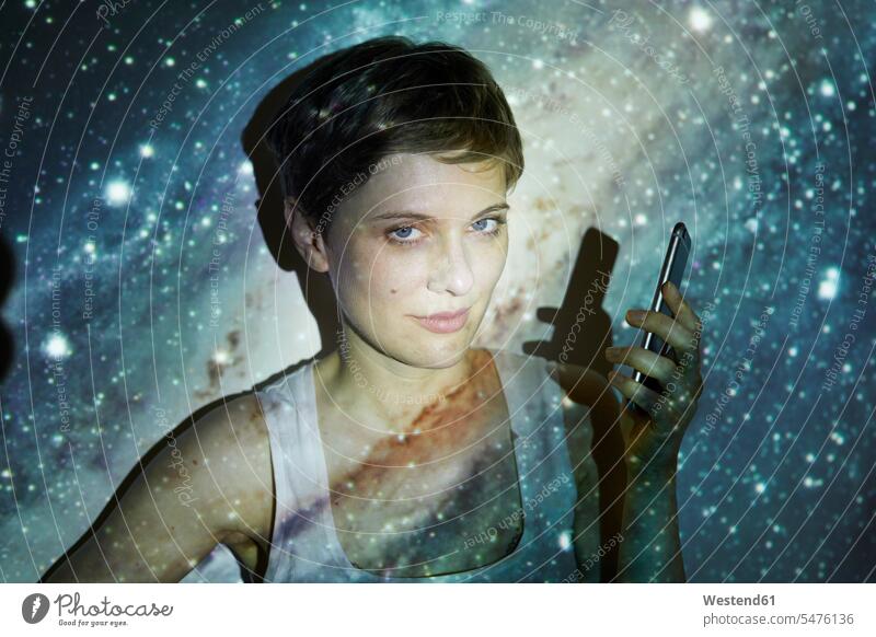 Porträt einer Frau, die ein Smartphone hält, Projektion eines Sternenhimmels Milchstraße Milchstrasse weiblich Frauen Blickkontakt Augenkontakt kurzhaarig