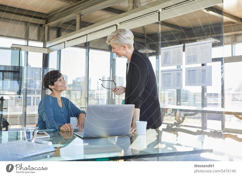 Zwei lächelnde Geschäftsfrauen diskutieren am Schreibtisch im Büro besprechen Besprechung Businesswomen Businessfrauen Businesswoman Office Büros Arbeitstisch