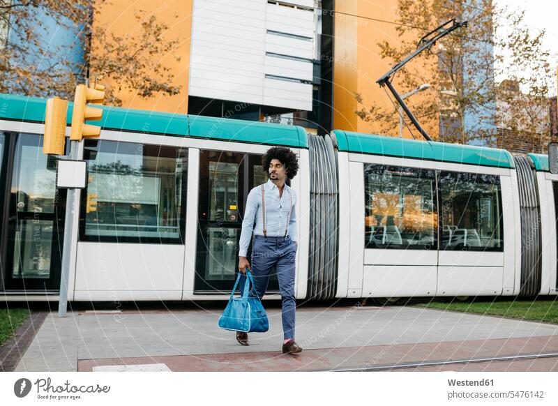 Spanien, Barcelona, Mann mit Tasche beim Überqueren der Straße vor einer Straßenbahn Strassen überqueren Taschen Trambahn S-Bahn S-Bahnen Strassenbahnen